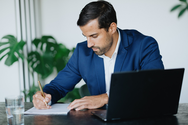 Foto von Steuerberater Sebastian Kößler, schreibt Text auf einen Block, vor ihm steht ein Laptop